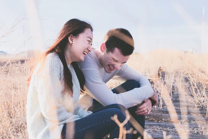 Couple sitting in field of dry grass laughing